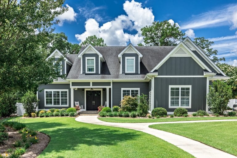 A large gray craftsman new construction house with a landscaped yard and leading pathway sidewalk